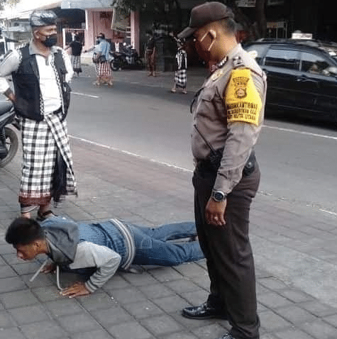 A local Balinese man lies on the street doing push-ups in front of a policeman for not wearing a facemask.