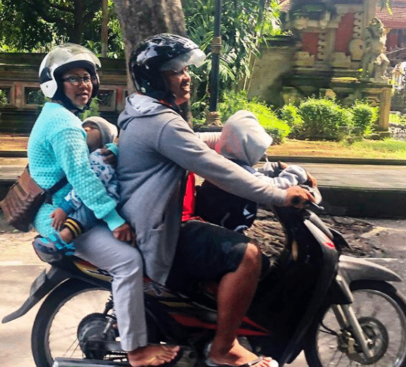 A Balinese mother and father, with two children, ride through Sanur, Bali, on a motorbike.