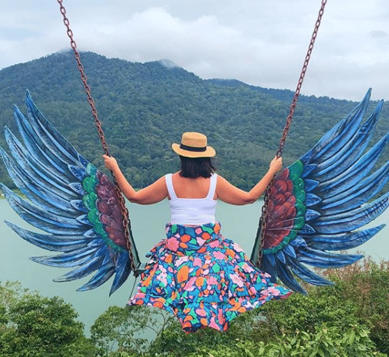 Karlie, enjoying an ornate swing overlooking the water and a coastal hillside in Ubud, Bali.