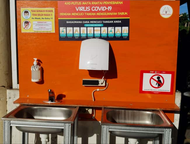 A handwashing station outside of a Balinese supermarket featuring warnings and recommendations to prevent the spread of COVID-19.