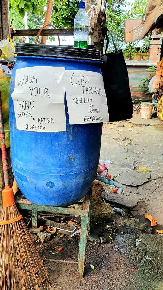 A water drum with signs in English and Bahasa advising locals to wash hands before and after shopping.